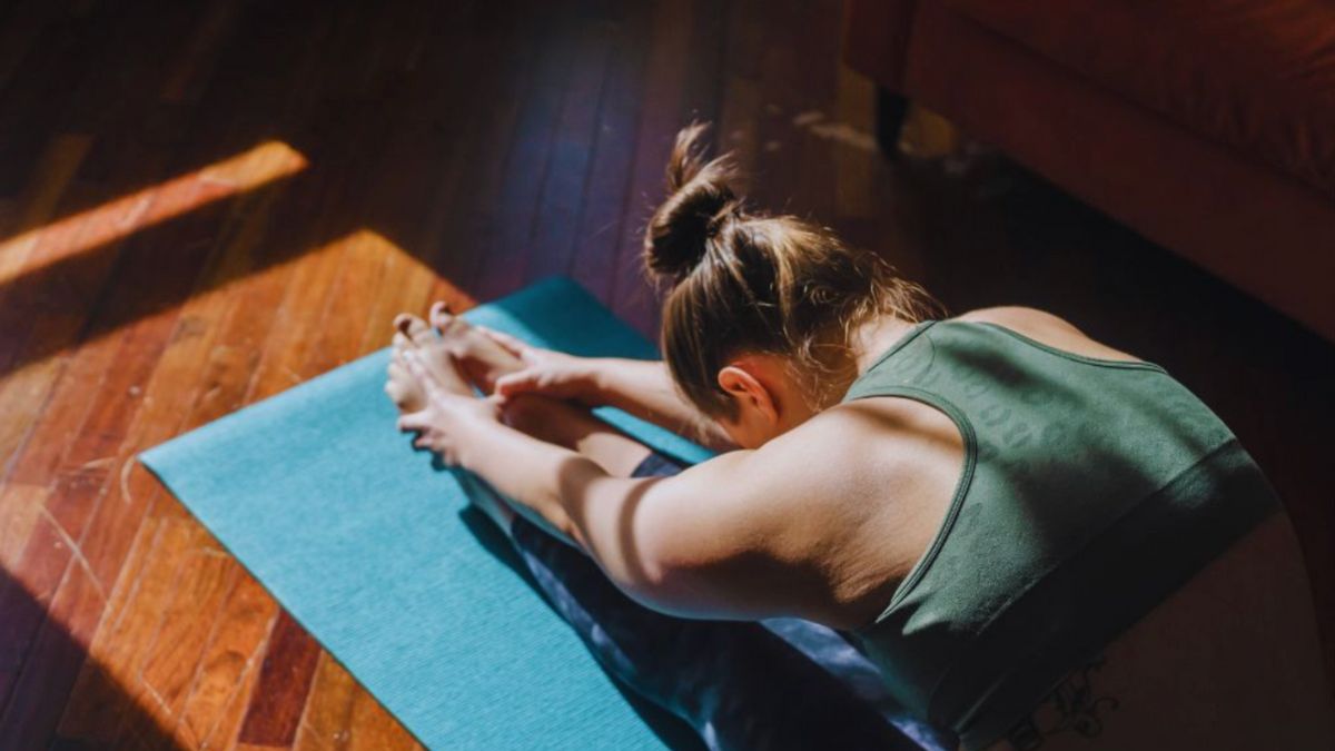 A woman in athletic wear stretches on a yoga mat in a sunlit room, showing how regular movement and gentle exercise may support mobility, wellness, and functional medicine strategies for managing rheumatoid arthritis and reducing inflammation.