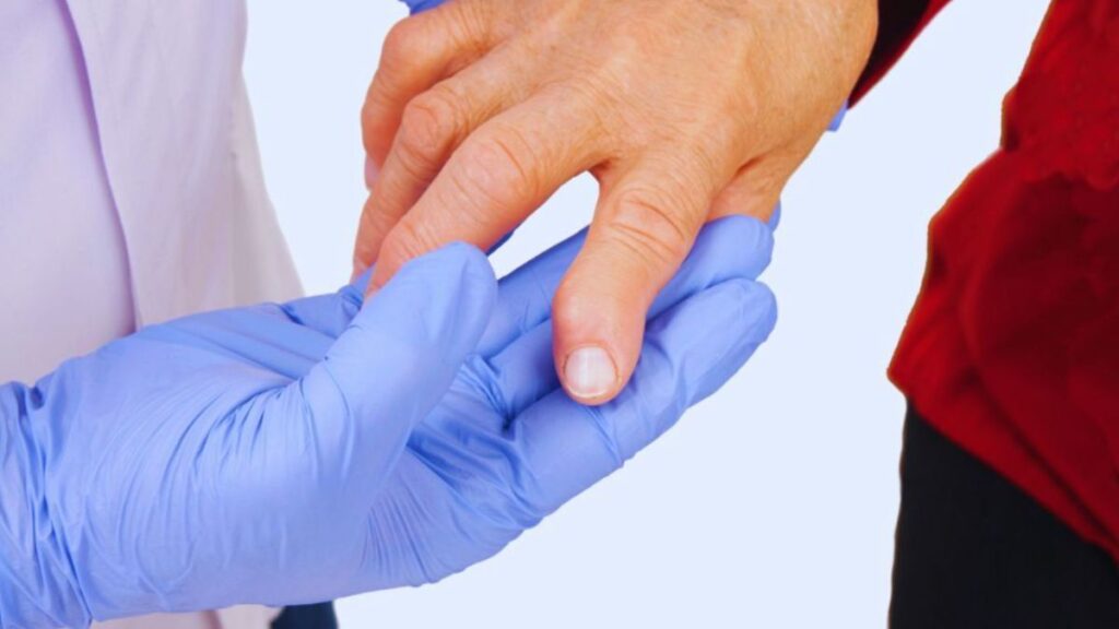 Autoimmune Doctor Near Me: How to Choose the Right One? 3 An autoimmune doctor wearing blue gloves gently examines an older adult’s hand, suggesting a medical evaluation for autoimmune conditions such as rheumatoid arthritis.