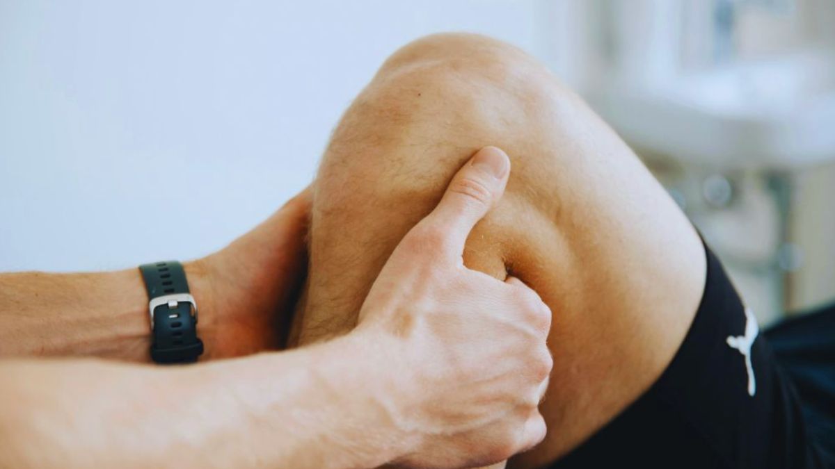 Miami Joint Pain Treatment: How Physical Therapy Can Help 5 A close-up image showing a person holding their knee with both hands, suggesting discomfort or joint pain. The individual is wearing a black sports watch and black athletic shorts, and the setting appears to be a clinical or rehabilitation environment, highlighting the concept of Miami joint pain treatment through physical therapy.
