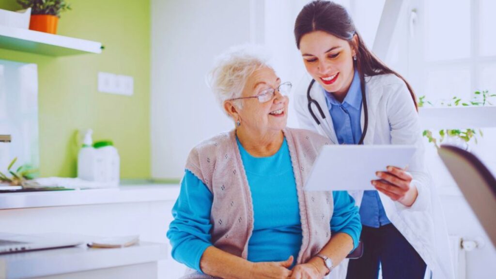 A functional doctor in Miami smiling and showing medical results on a digital tablet to an older woman during a consultation in a bright, modern clinic.