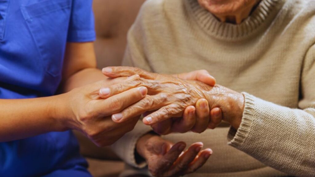 A nurse supports an elderly woman by holding her hand, emphasizing the caring nature of rheumatoid arthritis treatment in Brickell.
